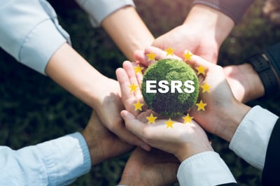 Plusieurs mains entourent et soutiennent une sphère recouverte de végétation portant le texte « ESRS », encadrée par les douze étoiles de l’Union européenne, symbolisant la collaboration autour des normes européennes de reporting de durabilité.