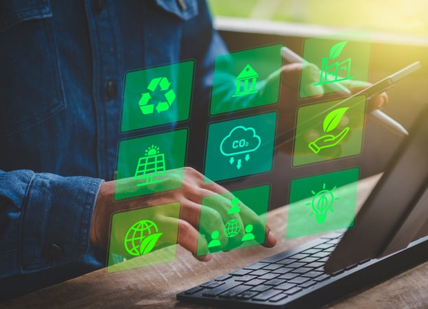 Personne utilisant une tablette et un clavier d’ordinateur, avec des icônes numériques vertes superposées représentant le recyclage, l’énergie solaire, la réduction des émissions de CO₂, la protection de l’environnement, l’innovation durable et la responsabilité sociale. L’image illustre la gestion ou le suivi d’initiatives de développement durable à l’aide d’outils numériques.