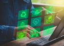 Personne utilisant une tablette et un clavier d’ordinateur, avec des icônes numériques vertes superposées représentant le recyclage, l’énergie solaire, la réduction des émissions de CO₂, la protection de l’environnement, l’innovation durable et la responsabilité sociale. L’image illustre la gestion ou le suivi d’initiatives de développement durable à l’aide d’outils numériques.