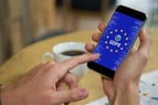Main tenant un smartphone affichant un écran sur le RGPD, avec un café en arrière-plan.