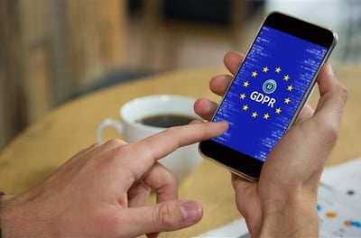 Main tenant un smartphone affichant un écran sur le RGPD, avec un café en arrière-plan.