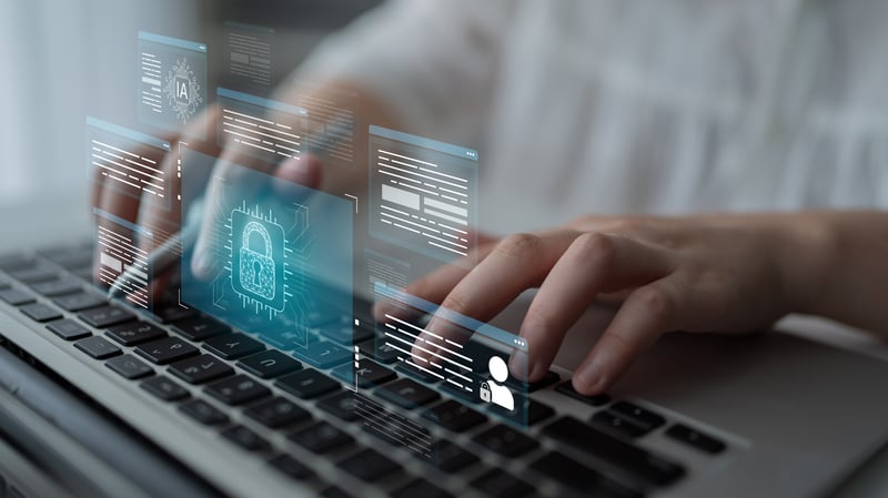 Main utilisant le clavier d’un ordinateur portable, avec des éléments graphiques numériques superposés représentant un cadenas et des interfaces de données, illustrant la cybersécurité et la protection des informations.