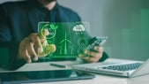 Personne utilisant un smartphone devant un ordinateur portable, avec une interface graphique verte superposée illustrant des thèmes de développement durable : « Net Zero », réduction du CO₂, éoliennes, planète tenue dans des mains et économie circulaire. L’image évoque le suivi ou la gestion numérique d’objectifs environnementaux.