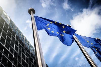 Drapeaux de l’Union européenne flottant au vent devant un bâtiment moderne, sous un ciel partiellement nuageux.