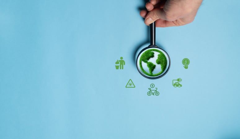Main tenant une loupe au-dessus d’un globe terrestre vert stylisé, entouré d’icônes liées au développement durable et à l’environnement (recyclage, mobilité électrique, énergie propre et gestion des déchets) sur un fond bleu clair.