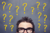 Personne avec des lunettes sous plusieurs points d’interrogation jaunes sur fond sombre.