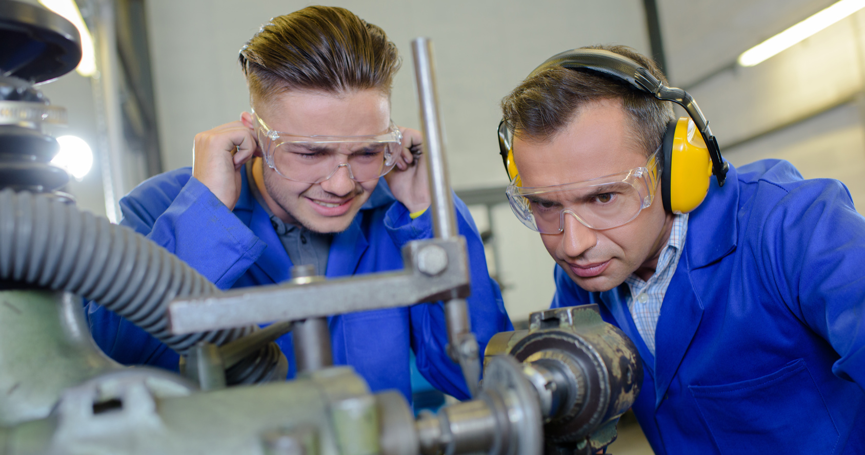 un homme avec des protections anti-bruit et un homme se bouchant les oreilles devant un machine bruyante